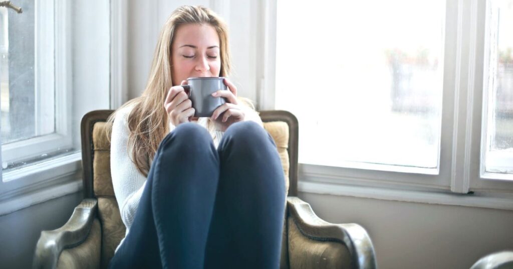 woman sipping tea in cozy chair with knees drawn up under chin